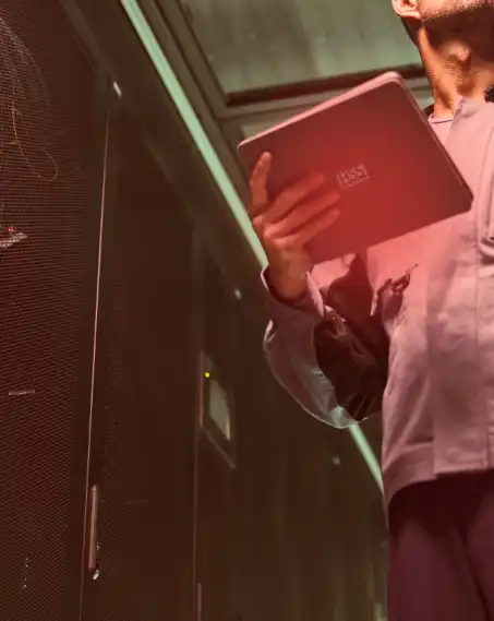 Homem segura tablet e cabo nas mãos em uma torre de servidores