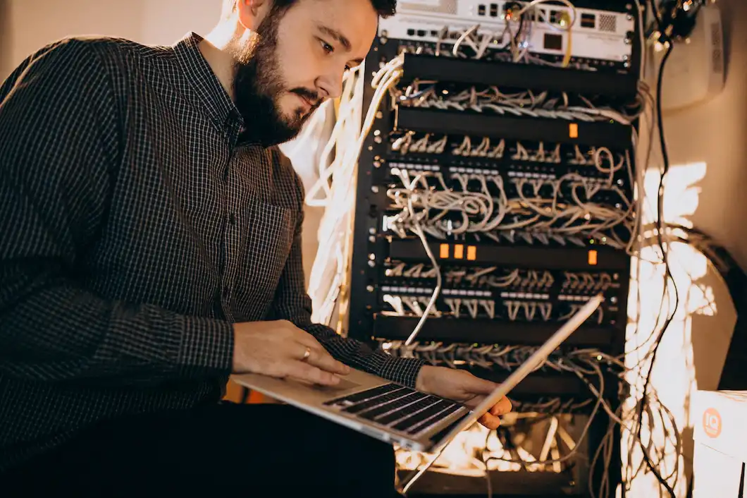 Homem jovem olha notebook em uma sala com switches